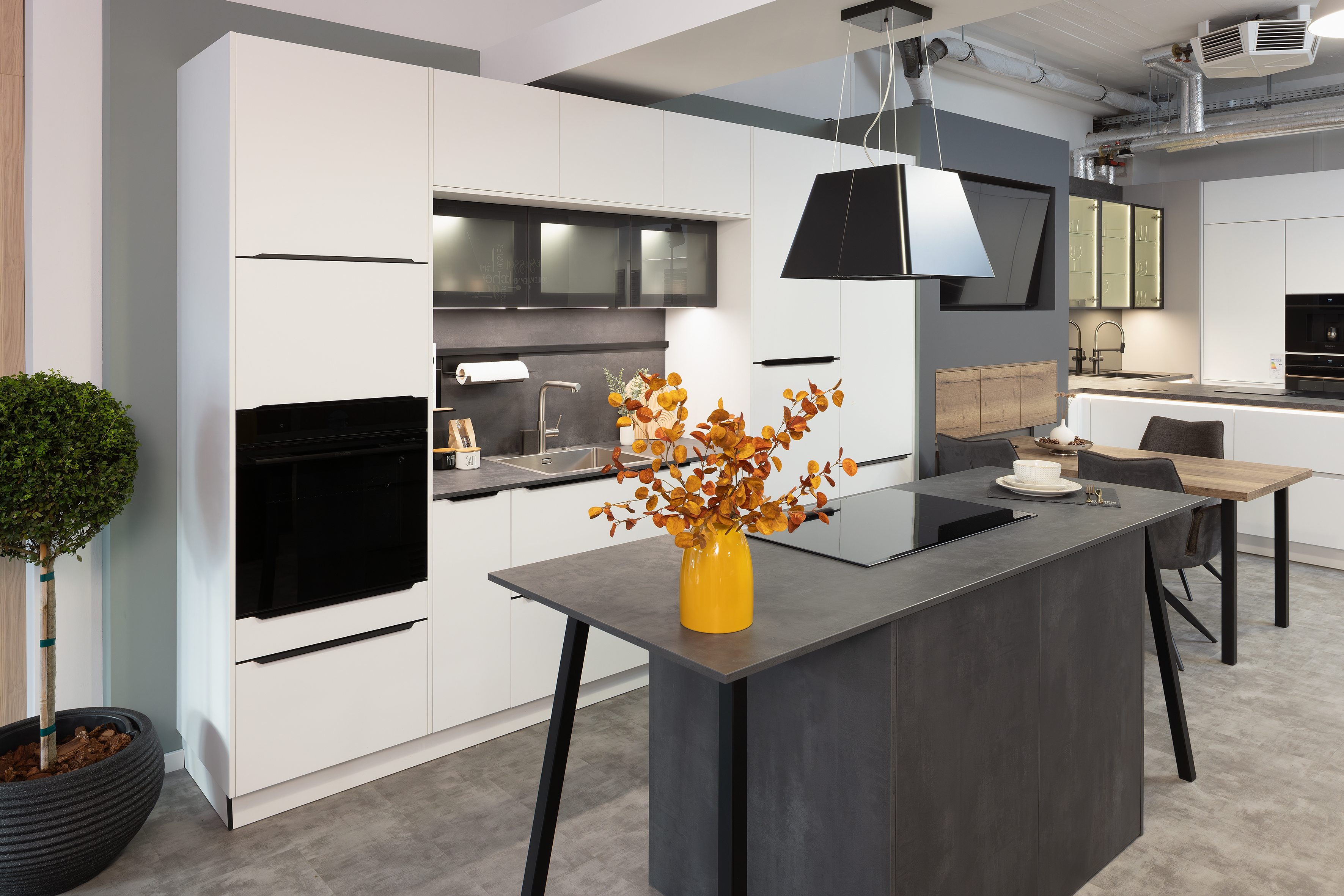 Moderne Küche mit Kochinsel, gelber Vase mit Zweigen und weißen Einbauschränken