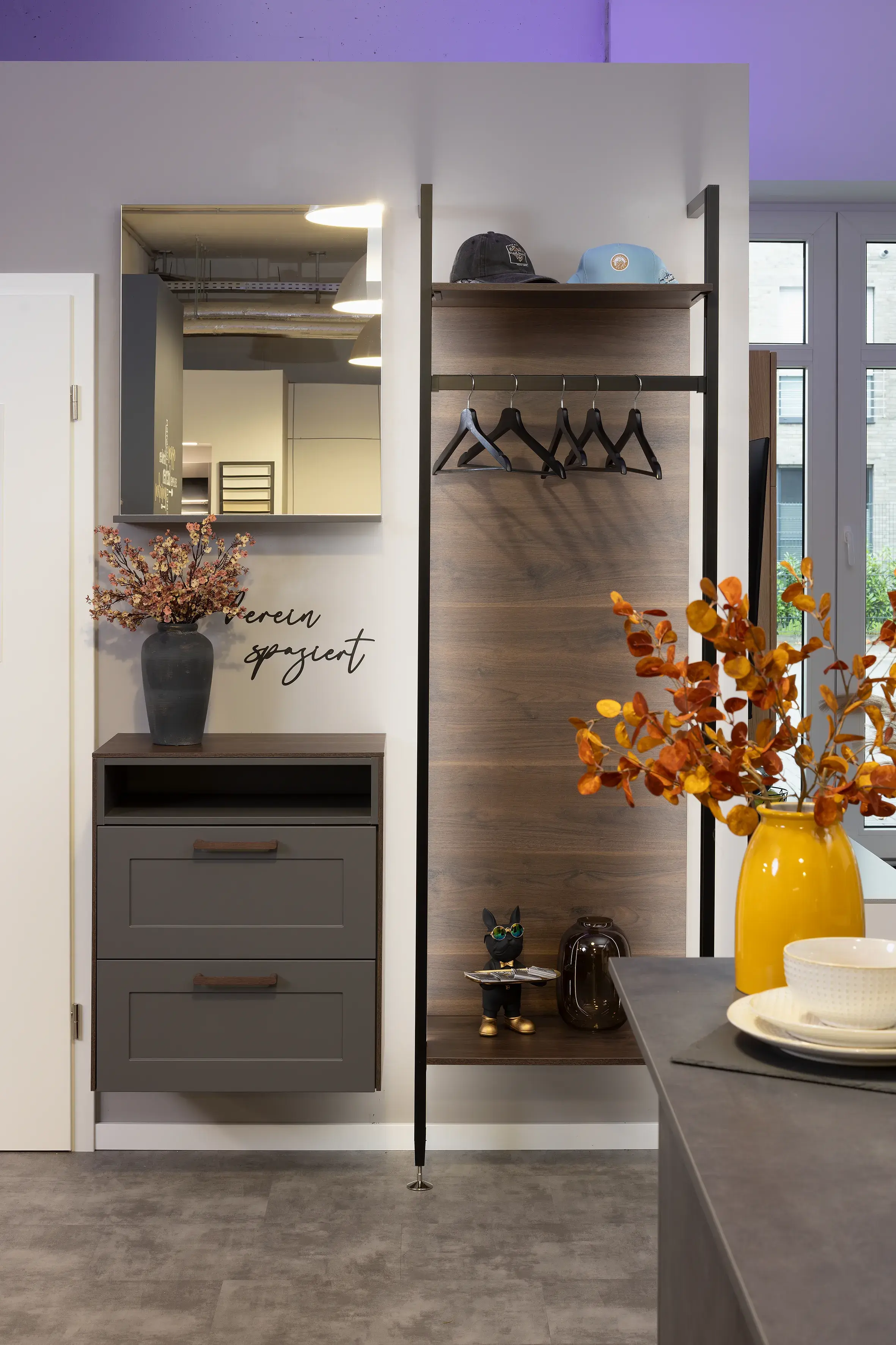 Moderner Flur mit Spiegel, Kommode, Garderobe und herbstlicher Blumendekoration.